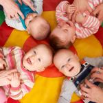 zwei Babys liegen lachend auf dem Rücken und werden gekitzelt