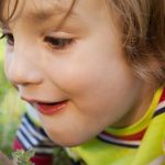 Kind beobachtet etwas im Gras durch ein Vergrößerungsglas