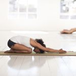 Eine Frau in der Hocke mit ausgestreckten Armen nach vorne auf die Matte