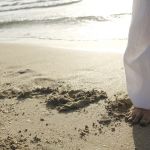 Ein Fuß im Sand, im Hintergrund Wasser